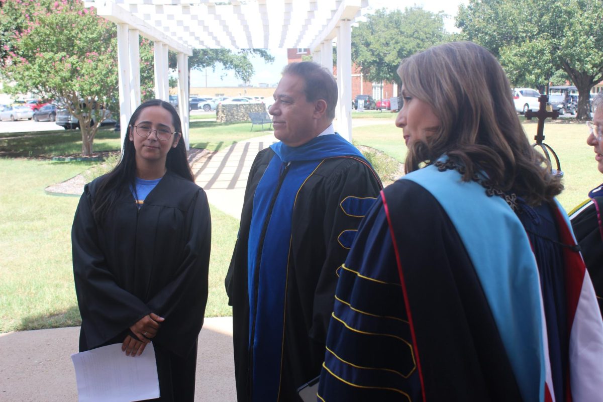 Dr. Emily Messer, Dr. Hector Quintanilla the Provost and Senior Vice President, and first-year representative Max Gusman share words as the procession is about to begin. 