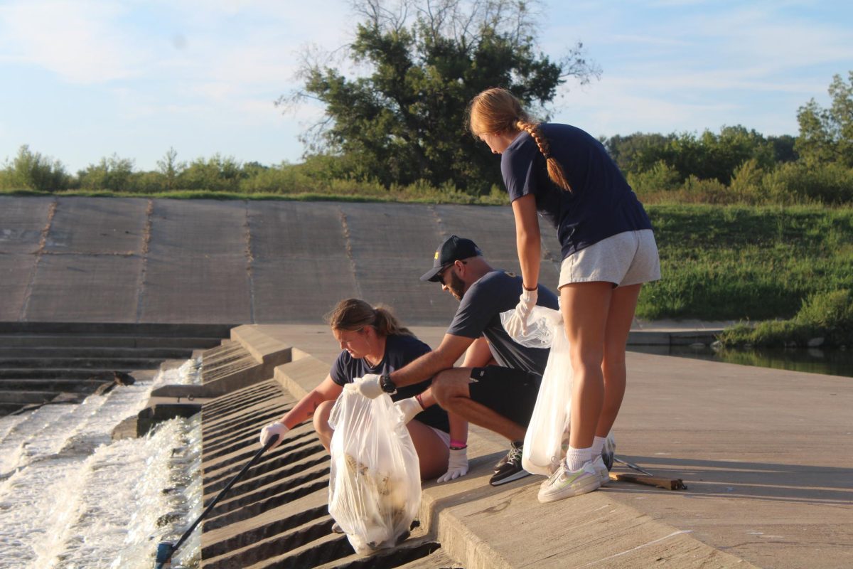 (From left) Reagan Fitzsimmons, first-year undecided major,  picks up trash while Jorge Rodriguez, women's beach volleyball player, and Mayara Swillens, junior exercise science major, assist her.