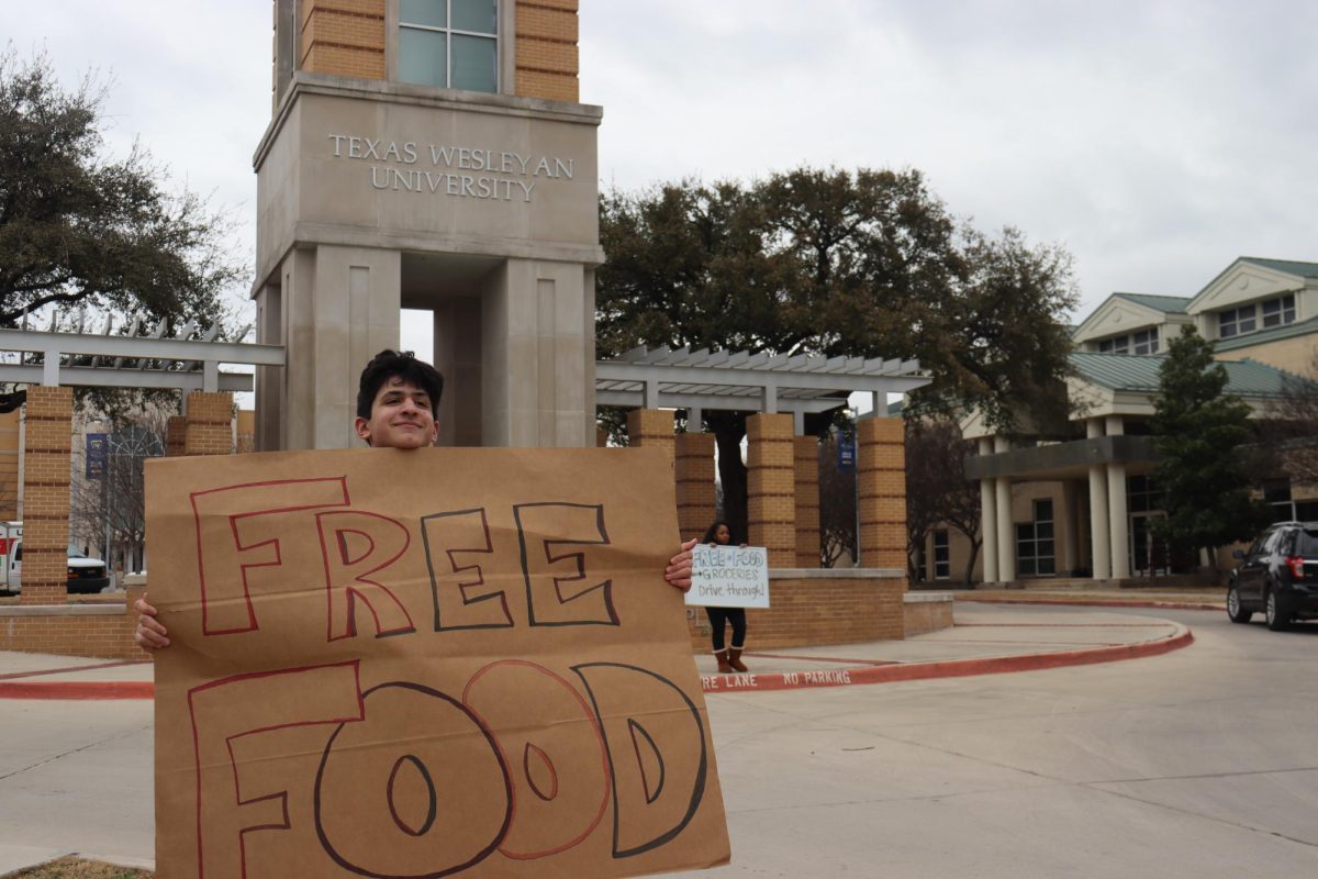 Volunteers Nicholas Dima and Keziah Selby hold signs in front of the Martin Center horseshoe, urging oncoming cars to stop for free groceries. 