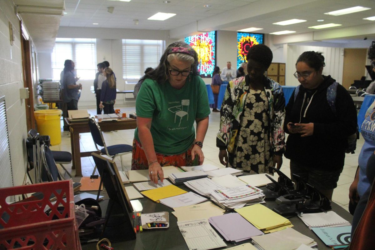 Students Emely Lopez and Aline Uwingabire watch on as Sara Zamora explains to students how to create a recycled scrap book.